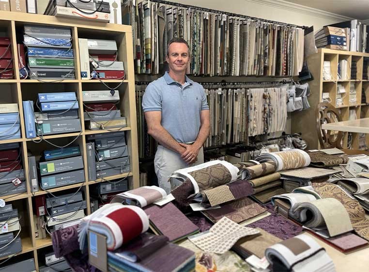 Man wearing a collard shirt standing by a desk covered in fabric samples